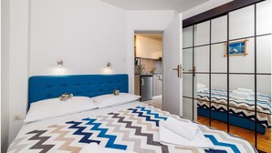 Un dormitorio con cabecera azul, colcha estampada y vistas a una cocina y un baño a través de una puerta de cristal.