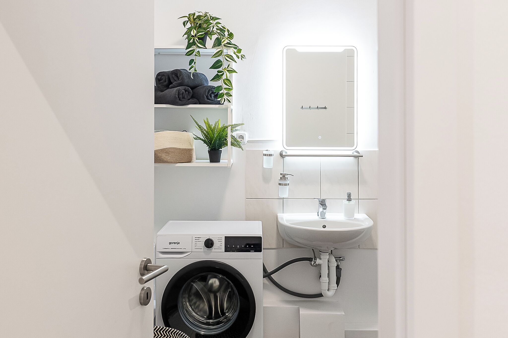 Une salle de bain moderne et compacte, dotée d’un lave-linge encastré, d’un lavabo et d’un miroir.