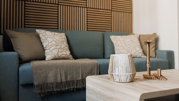 A modern living room with a blue sofa, patterned cushions, a wooden coffee table, and a decorative lamp. - Apart Brunnen Bremerhaven (Bremerhaven)