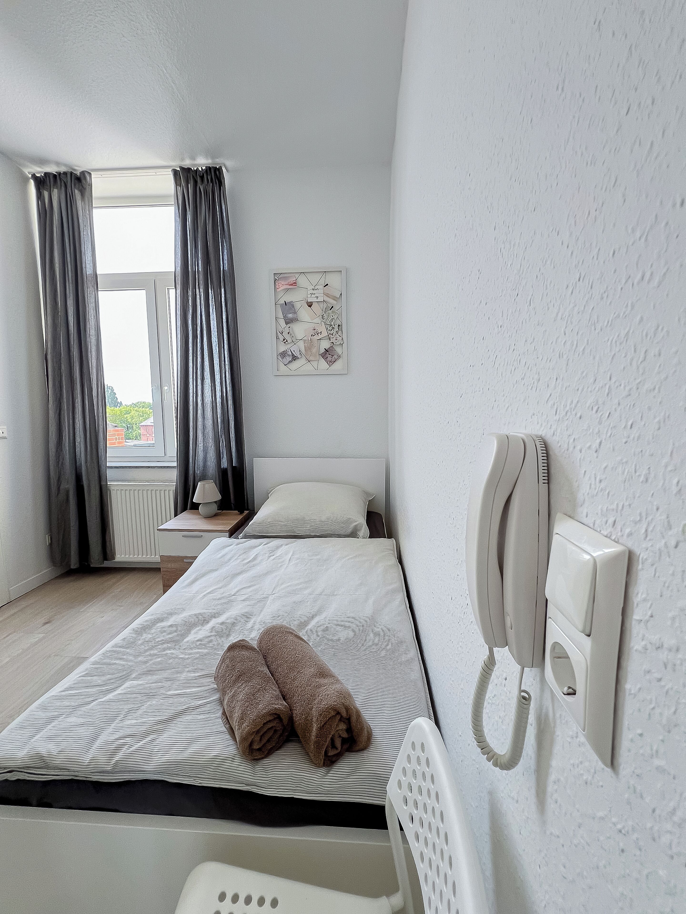 Une chambre d’hôtel avec un lit, une table de chevet avec une lampe, un téléphone et une fenêtre avec des rideaux.