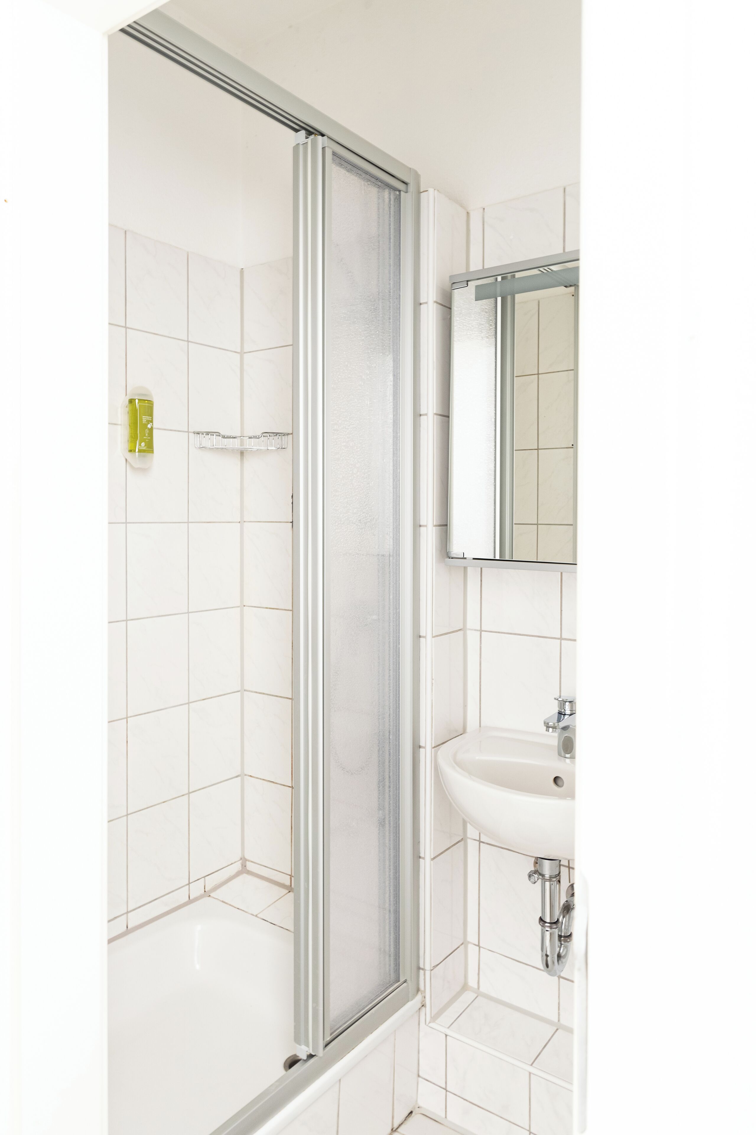 Een badkamer met een douchecabine, een wastafel en een spiegel.