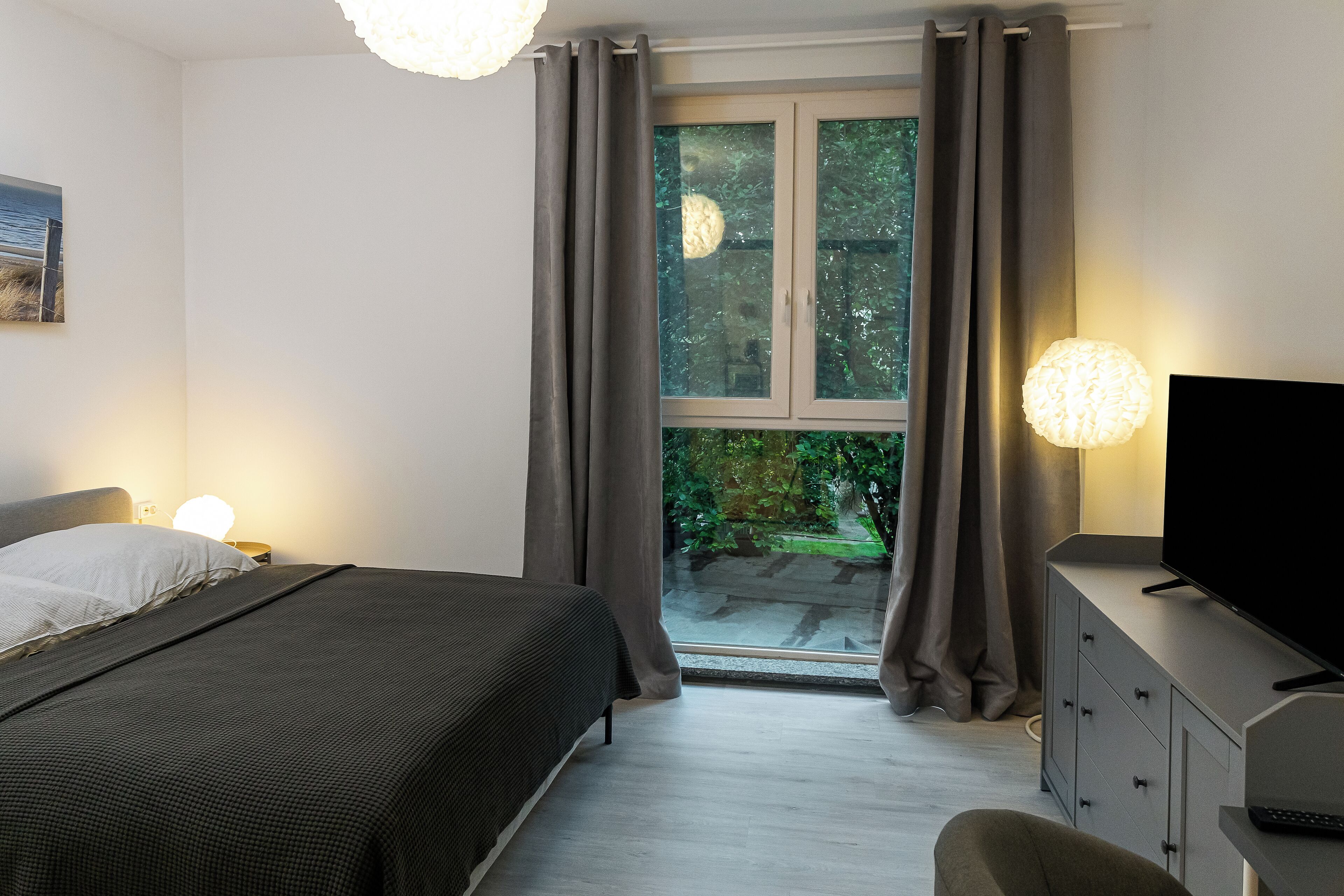Un dormitorio con cama, televisor, cómoda y ventana con cortinas.