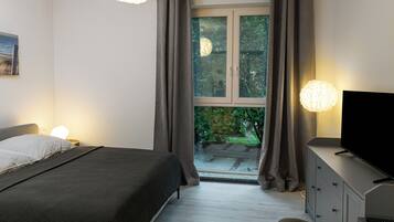 Un dormitorio con cama, televisor, cómoda y ventana con cortinas.