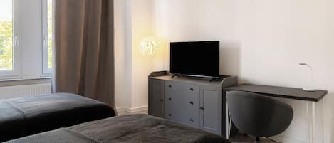 Ein Schlafzimmer mit zwei Betten, einem Schreibtisch mit Stuhl, einem Fernseher und einer Lampe.