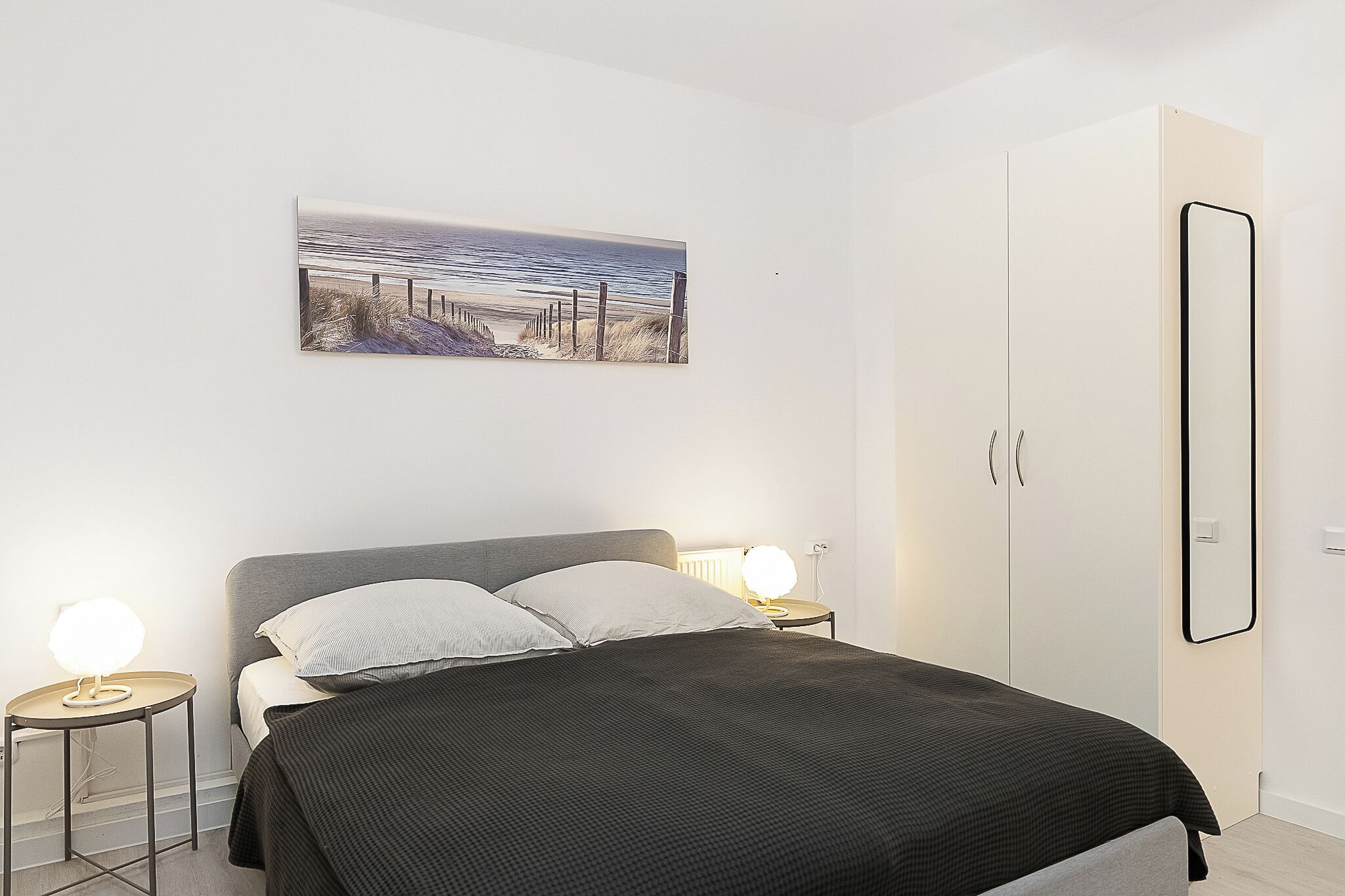 A bedroom with a bed, bedside tables, a nightstand, a wardrobe, and a painting on the wall.