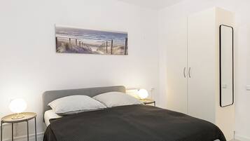 A bedroom with a bed, bedside tables, a nightstand, a wardrobe, and a painting on the wall.
