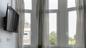A bedroom with a bed, a TV mounted on the wall, a small table with a chair, and a window with curtains. - Apart Brunnen Bremerhaven (Bremerhaven)
