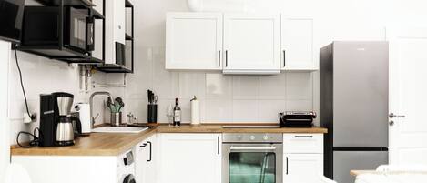 A modern kitchen with white cabinets, a stainless steel refrigerator, a built-in oven, and a coffee maker.