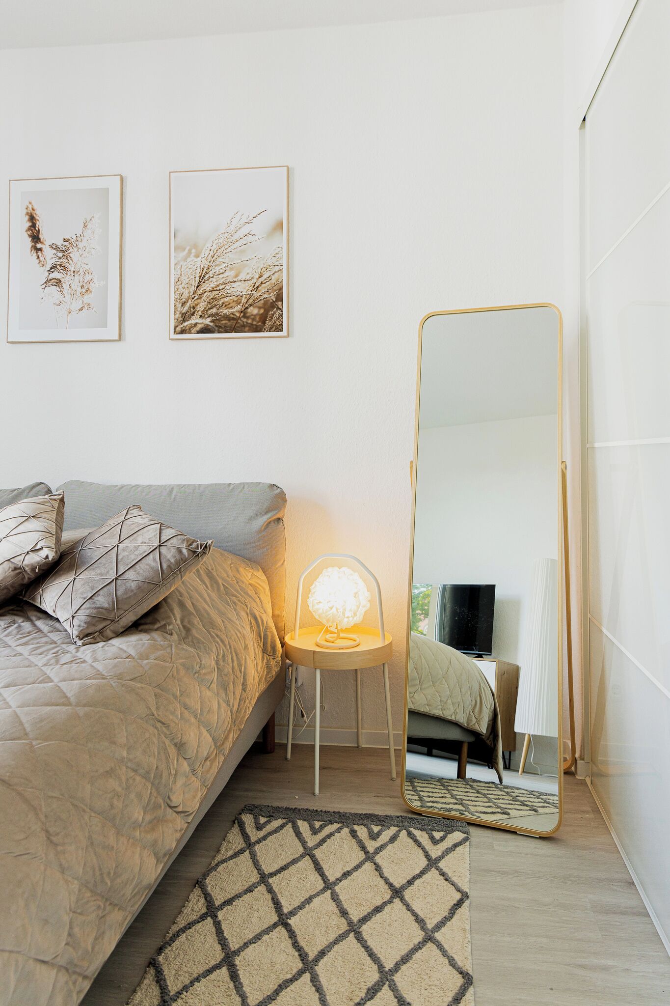 A bedroom with a bed, a standing mirror, and two framed pictures on the wall.