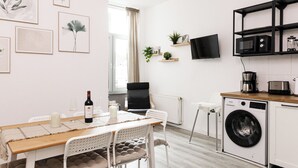 A modern kitchen with a washing machine, a dining table with chairs, and a TV mounted on the wall. - Apart Brunnen Bremerhaven (Bremerhaven)