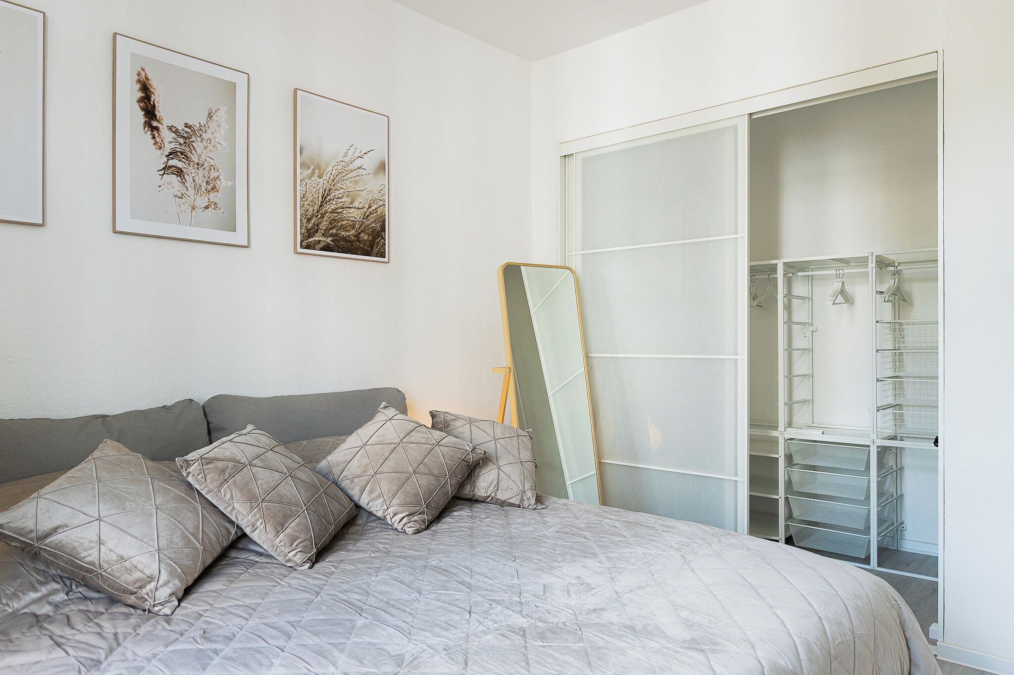 Una camera da letto con un letto, cuscini, un armadio e due quadri appesi al muro.