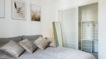 Een slaapkamer met een bed, kussens, een kledingkast en twee foto’s in lijsten aan de muur.