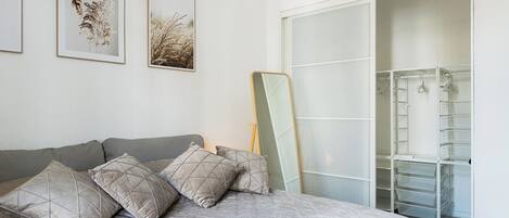 Una camera da letto con un letto, cuscini, un armadio e due quadri appesi al muro.