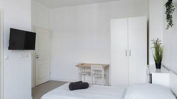 Een minimalistische slaapkamer met een bed, een bureau, twee stoelen, een televisie en een potplant.