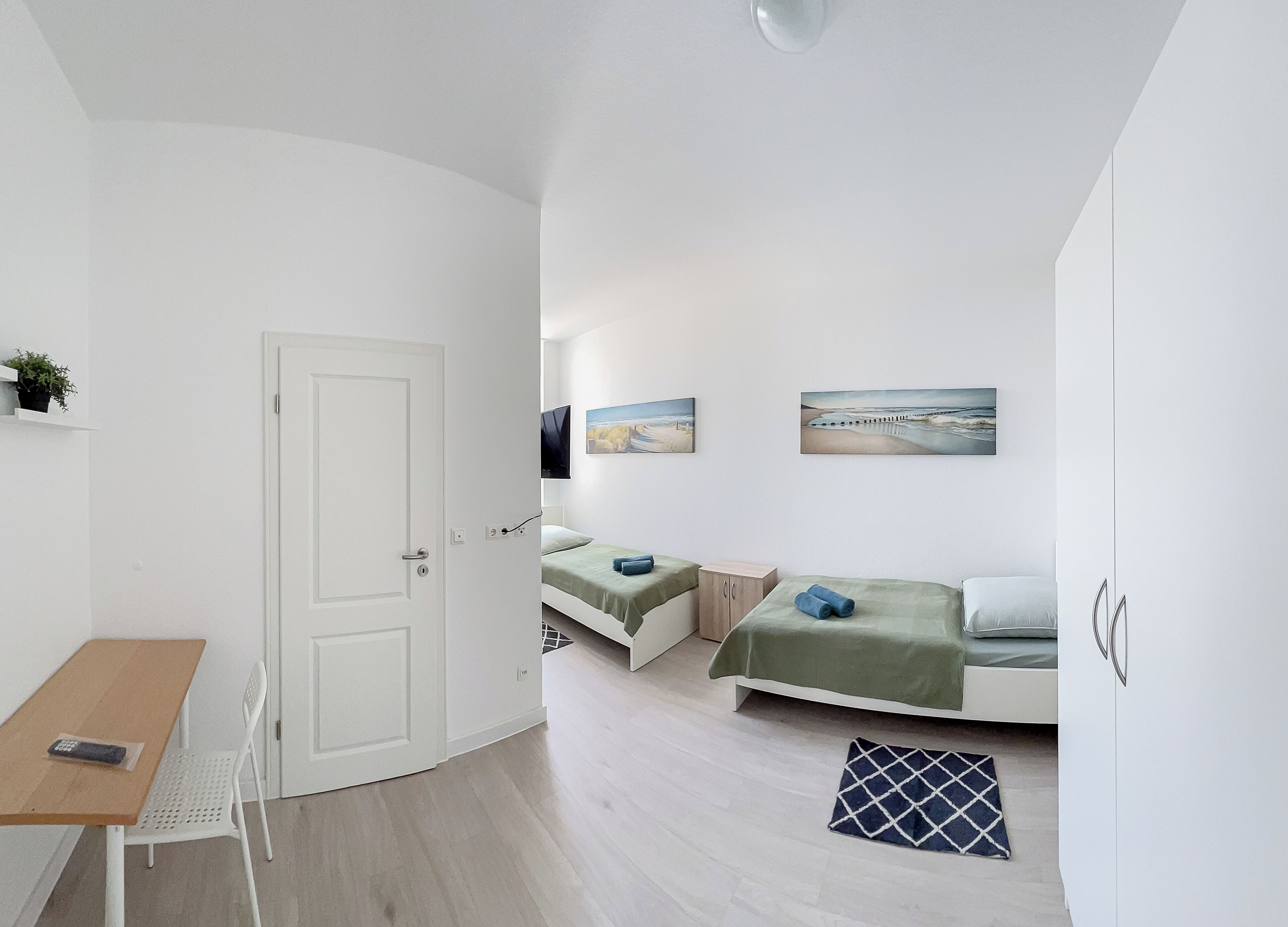 A compact room with a bed, a small desk, and a chair. There are two paintings on the wall.