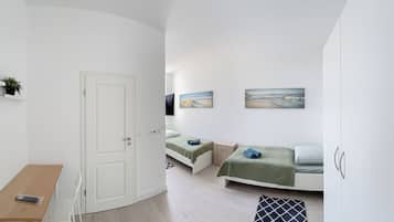 A compact room with a bed, a small desk, and a chair. There are two paintings on the wall.