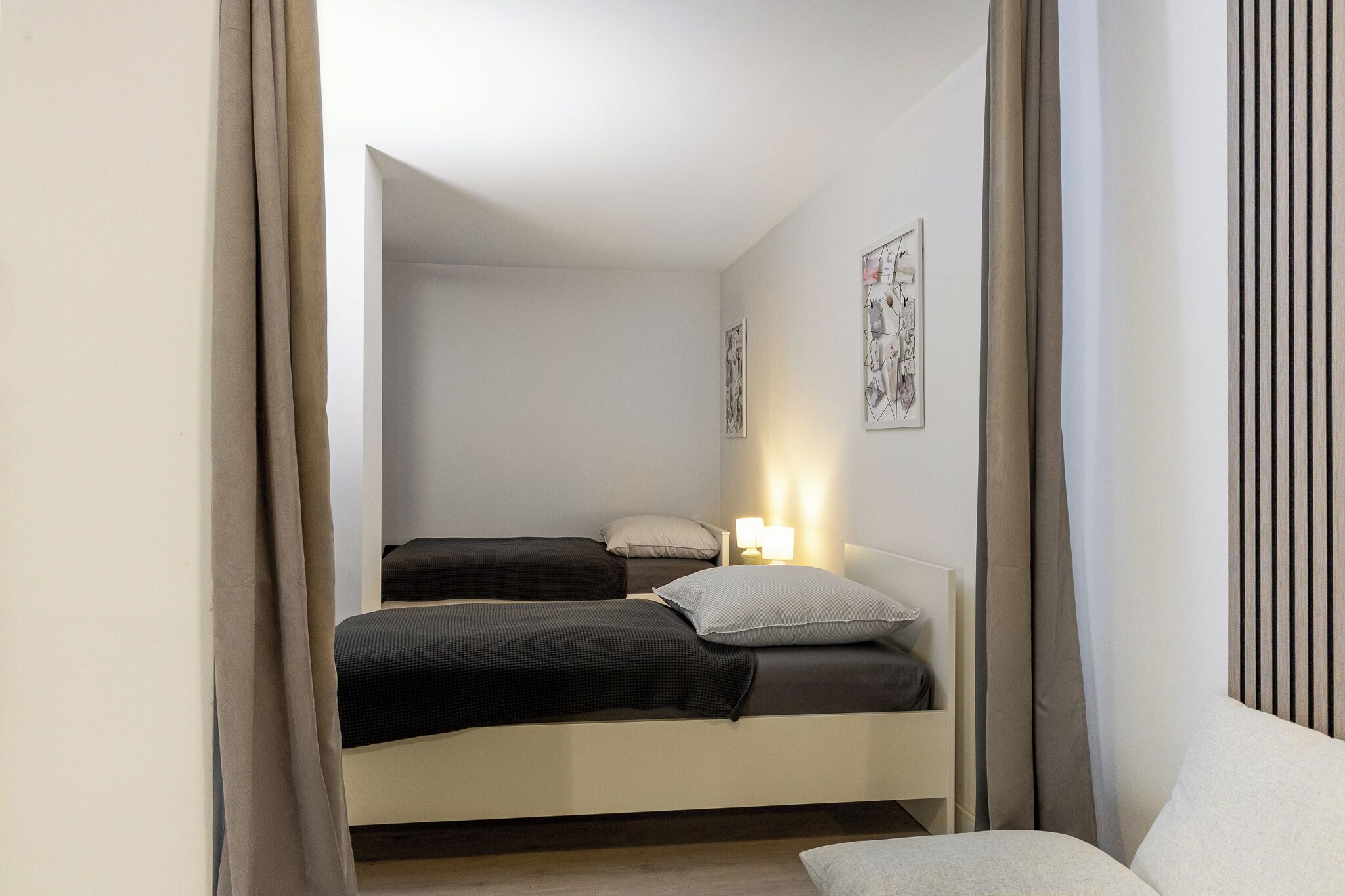A bedroom with two beds, a bedside table with a lamp, and a wall-mounted artwork.