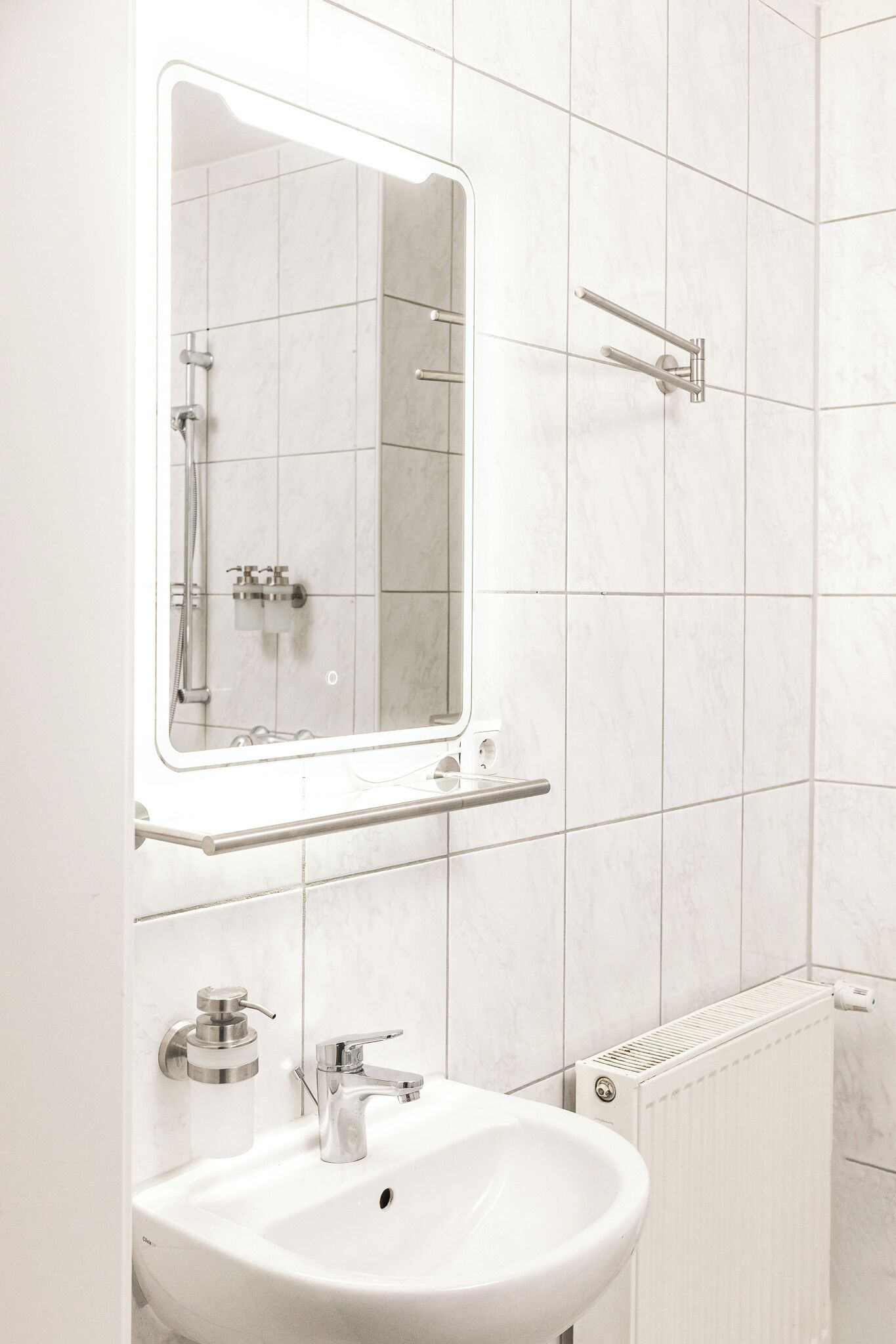 Un baño moderno con un lavamanos blanco, un espejo y una zona de ducha.