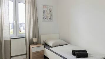 Un dormitorio con cama, mesita de noche, ventana con cortinas y una obra de arte colgada en la pared.