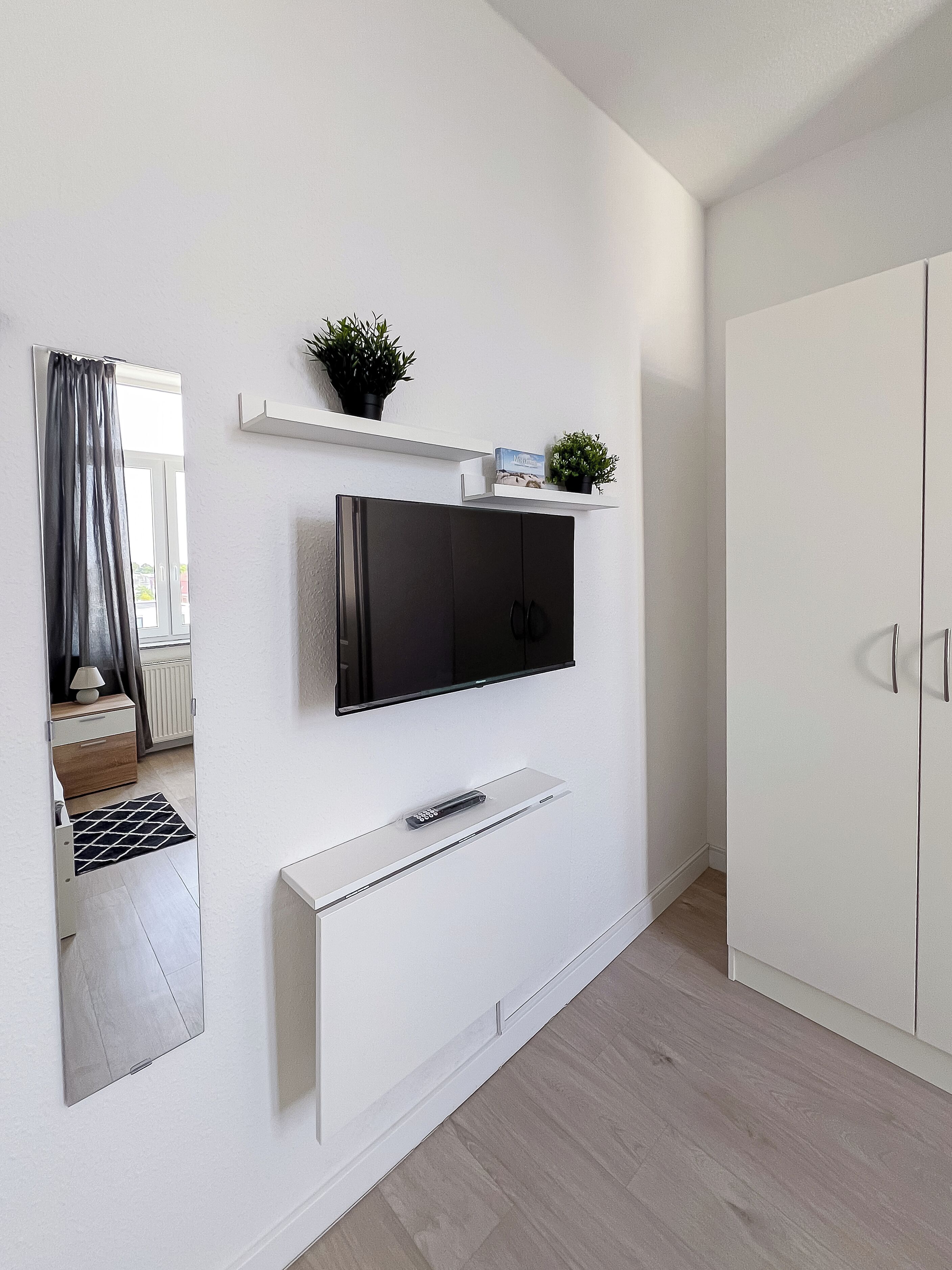 Una habitación moderna con un televisor de pantalla plana montado en la pared, un armario blanco y un estante pequeño con objetos decorativos.