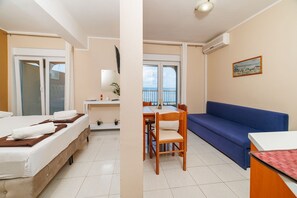 A hotel room with two beds, a desk with a chair, a balcony with a table, and a blue sofa. - Comfortable flat just 350 metres from the beach with sea views, pool, outdoor shower (Dramalj)