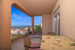 A balcony with a table and chairs, a view of the sea, and a building in the background. - Comfortable flat just 350 metres from the beach with sea views, pool, outdoor shower (Dramalj)