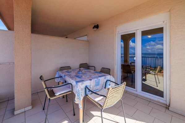 Un balcón con mesa y sillas, vista al mar y una puerta corrediza de cristal.