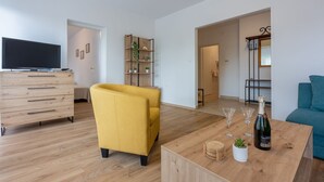 A modern living room with a wooden floor, a yellow armchair, a wooden coffee table with glasses and a bottle, and a blue sofa. - Idyllic flat just 250 metres from the beach with sea views, private terrace, private parking space (Crikvenica)