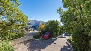 A red car parked in a driveway with a stone wall and greenery on the sides. - Idyllic flat just 250 metres from the beach with sea views, private terrace, private parking space (Crikvenica)