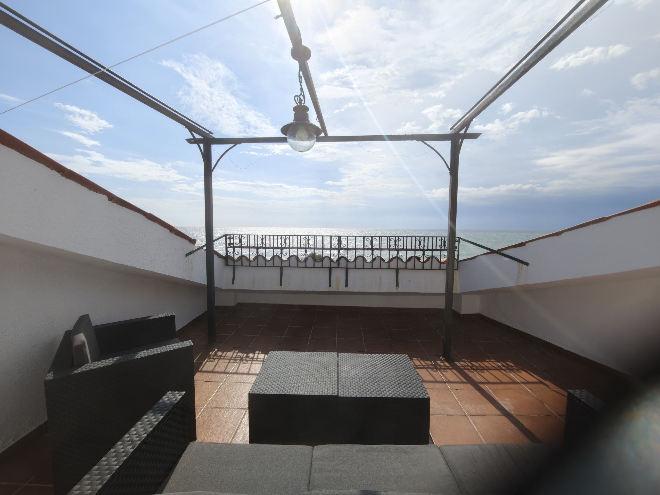 Una terraza en la azotea con barandilla de metal, un colgante de luz y vistas al mar.