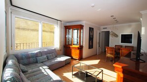 A living room with a sofa, a glass coffee table, a wooden cabinet, and a dining area with chairs and a table. - Masnou Chill - Penthouse Terrace in front of the Beach (El Masnou)