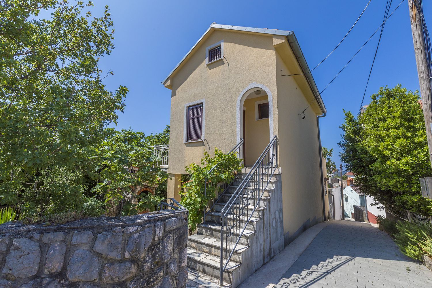 A two-story building with a stone wall, a staircase, and a clear sky.