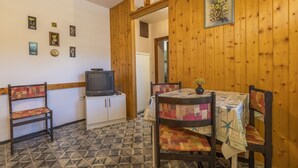 Une petite pièce agréable, avec un mur en bois, un téléviseur posé sur un meuble, une table entourée de chaises et un sol à motifs.
