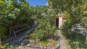 Un jardin avec un banc, un mur de pierre et un bâtiment doté d’un toit en tuiles.