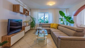 A modern living room with a flat-screen TV, a glass coffee table, a beige sofa, and a large window with curtains. - Fantastic flat with its own wine cellar, hydromassage shower, sea view - only 480 metres to the beach (Crikvenica)