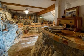 A rustic kitchen with stone walls, wooden beams, and a variety of kitchenware and utensils.