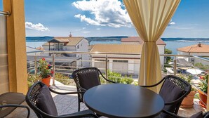 Ein Balkon mit Tisch und Stühlen, der auf eine Küstenstadt mit Häusern mit Terrakotta-Dächern und Blick aufs Meer blickt.
