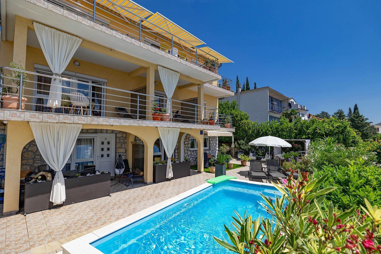 A two-story building with a pool, outdoor seating, and potted plants.