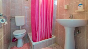 Un baño con inodoro, ducha con cortina rosa, lavamanos y un cubo de basura azul.