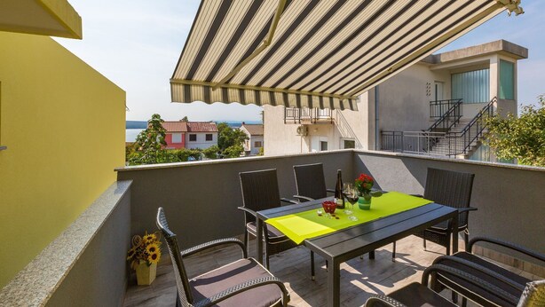Un balcón con una mesa y sillas, un toldo a rayas y vistas a edificios y al mar.