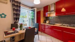 A modern kitchen with red cabinets, a gas stove, and a dining area with a table and chairs. - Mediterranean flat with three terraces, barbecue, WiFi - only 500 metres to the beach (Crikvenica)