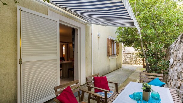 A patio area with a table set for dining, wooden chairs with cushions, and a striped awning providing shade. - Mediterranean flat with three terraces, barbecue, WiFi - only 500 metres to the beach (Crikvenica)