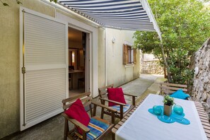 A patio area with a table set for dining, wooden chairs with cushions, and a striped awning providing shade. - Mediterranean flat with three terraces, barbecue, WiFi - only 500 metres to the beach (Crikvenica)