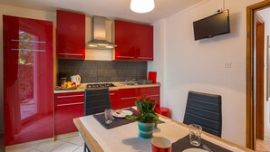 A modern kitchen with red cabinets, a gas stove, and a dining area with a table set for two. - Mediterranean flat with three terraces, barbecue, WiFi - only 500 metres to the beach (Crikvenica)