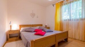 A bedroom with a wooden bed, a nightstand with a lamp, and a window with yellow curtains. - Mediterranean flat with three terraces, barbecue, WiFi - only 500 metres to the beach (Crikvenica)