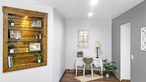 A hallway with a wooden shelf unit, a desk with a heart-shaped chair, and a lamp. - Colorado Willow House (Cortez)