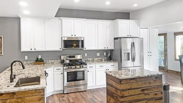 A modern kitchen with white cabinets, stainless steel appliances, and a wooden island. - Colorado Willow House (Cortez)