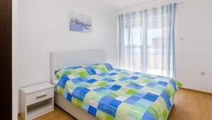 A bedroom with a bed, a nightstand, a window with sheer curtains, and a wall-mounted picture. - Idyllic flat just 400 metres from the sandy beach with sea views, WiFi and private parking (Crikvenica)