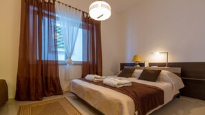 A neatly made bed with a brown headboard, a bedside lamp, and a window with curtains.
