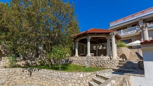 A stone-walled garden with a gazebo, steps leading to a building with a red-tiled roof.